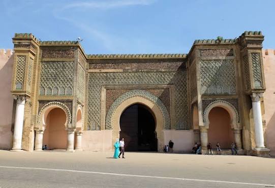 Bab Mansour — the great triumphal gate of Meknes, completed in 1732 under Sultan Moulay Ismail, its facade covered in green-and-white zellij tilework, fluted pilasters and a band of Kufic inscription that together make it one of the most imposing monumental gateways in North Africa